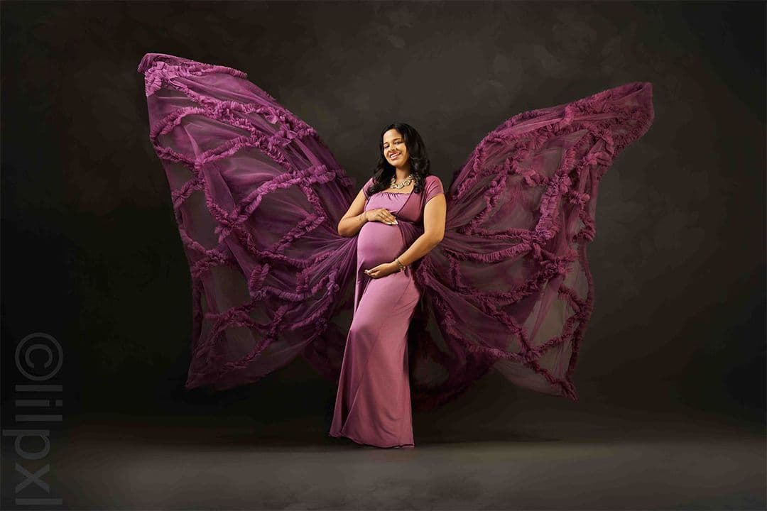Fine-art maternity portrait in a flowing purple gown, studio lighting